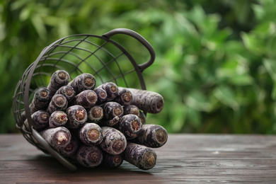 Raw black carrots in basket on wooden table against blurred background. Space for text