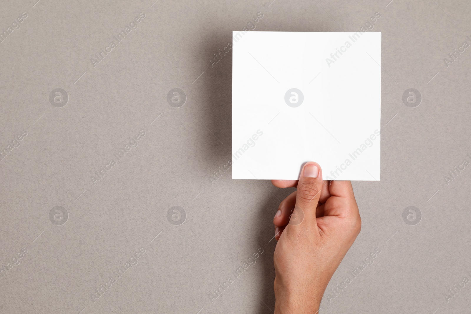 Photo of Man holding sheet of paper on grey background, closeup. Mockup for design