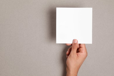 Man holding sheet of paper on grey background, closeup. Mockup for design