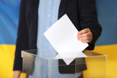 Photo of Woman putting voting paper into ballot box against Ukrainian flag, closeup