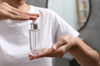 Photo of Woman with bottle of cosmetic serum on blurred background, closeup