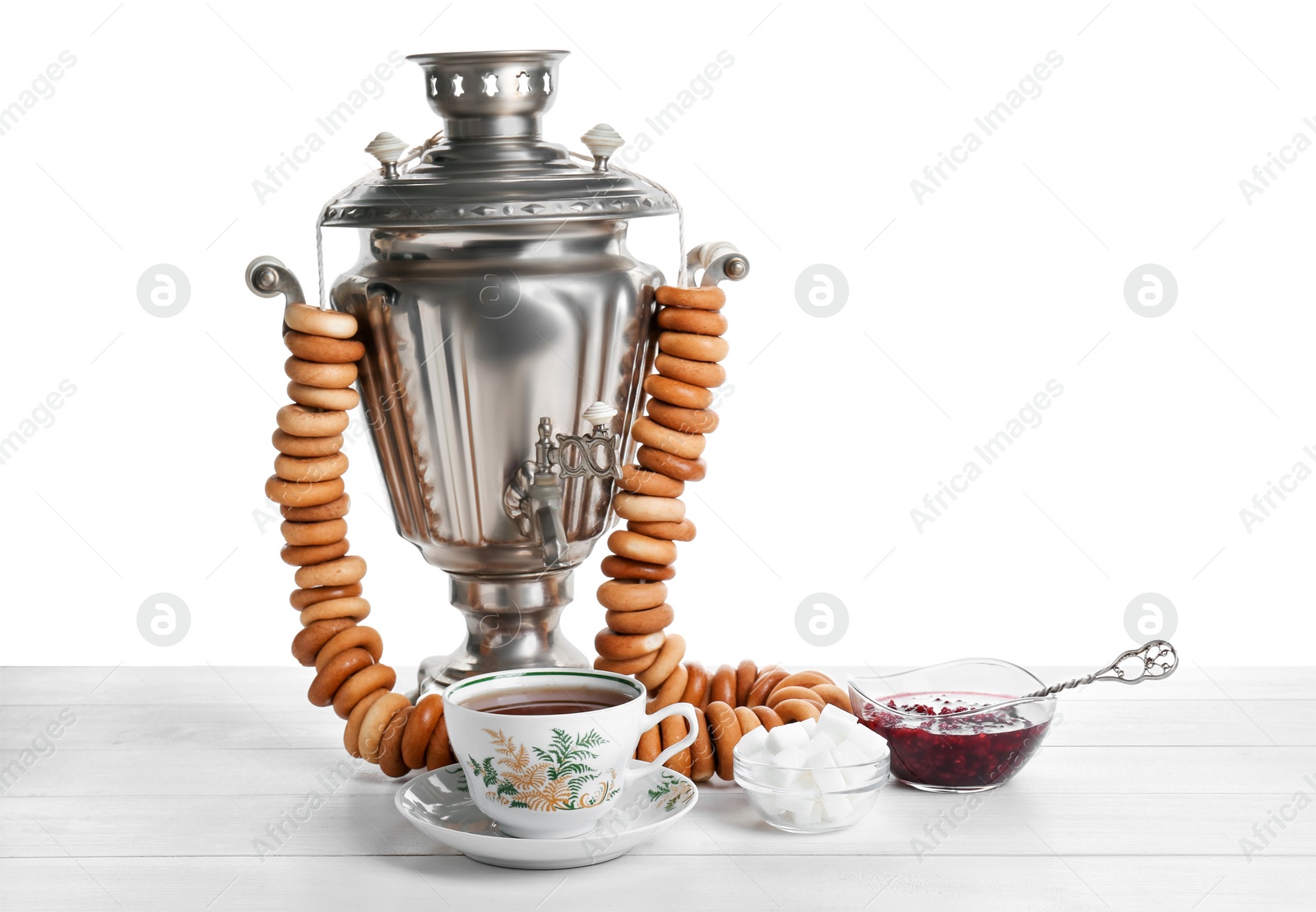 Photo of Samovar with hot tea, jam and delicious ring shaped Sushki (dry bagels) on table against white background