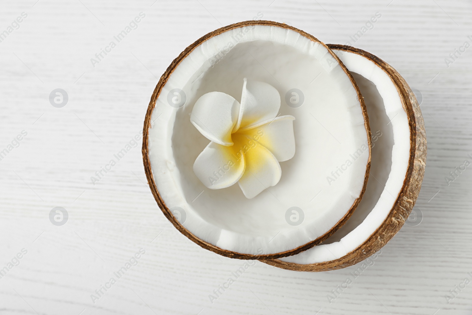 Photo of Halves of coconut and flower on white wooden background