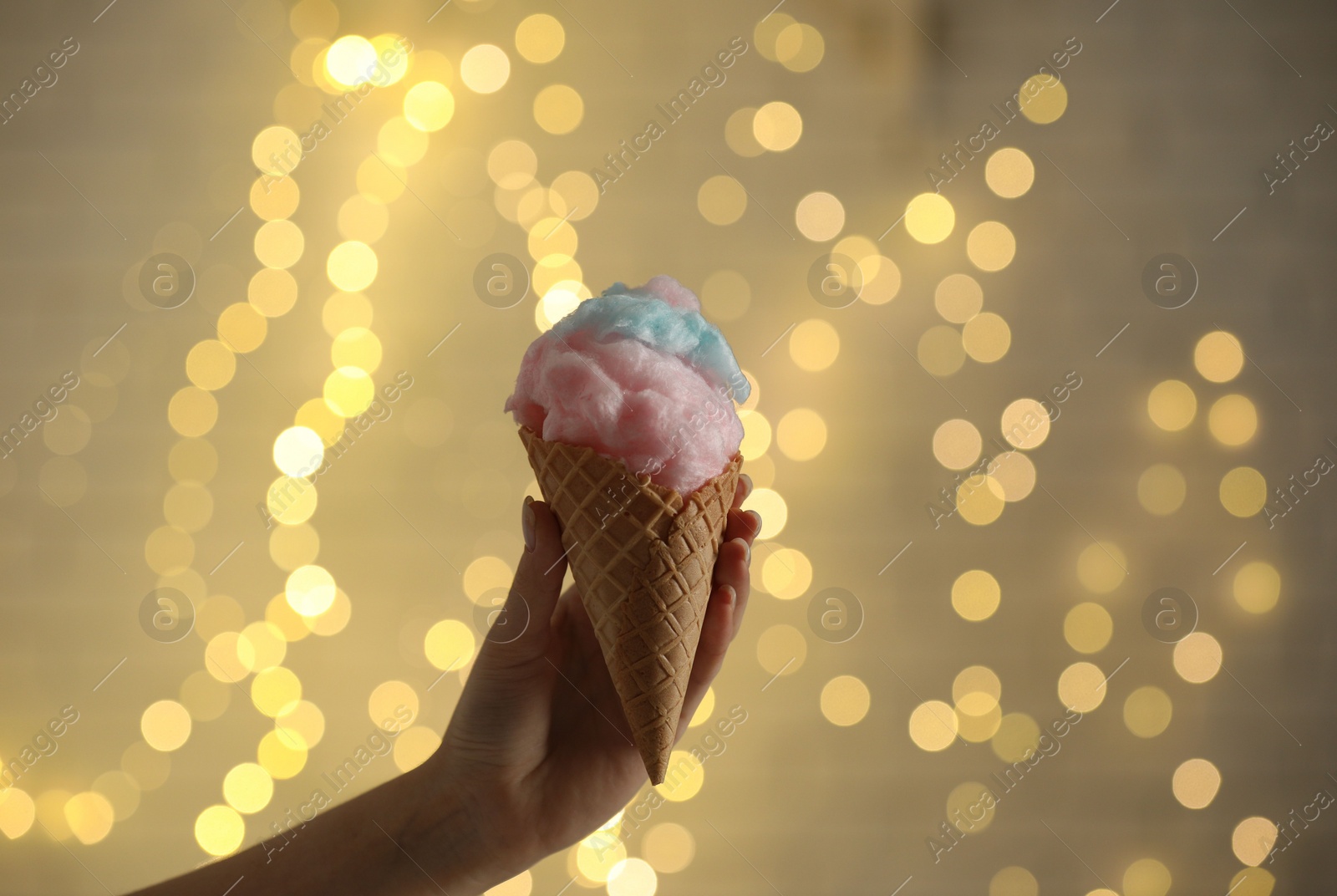 Photo of Woman holding waffle cone with cotton candy against blurred lights, closeup