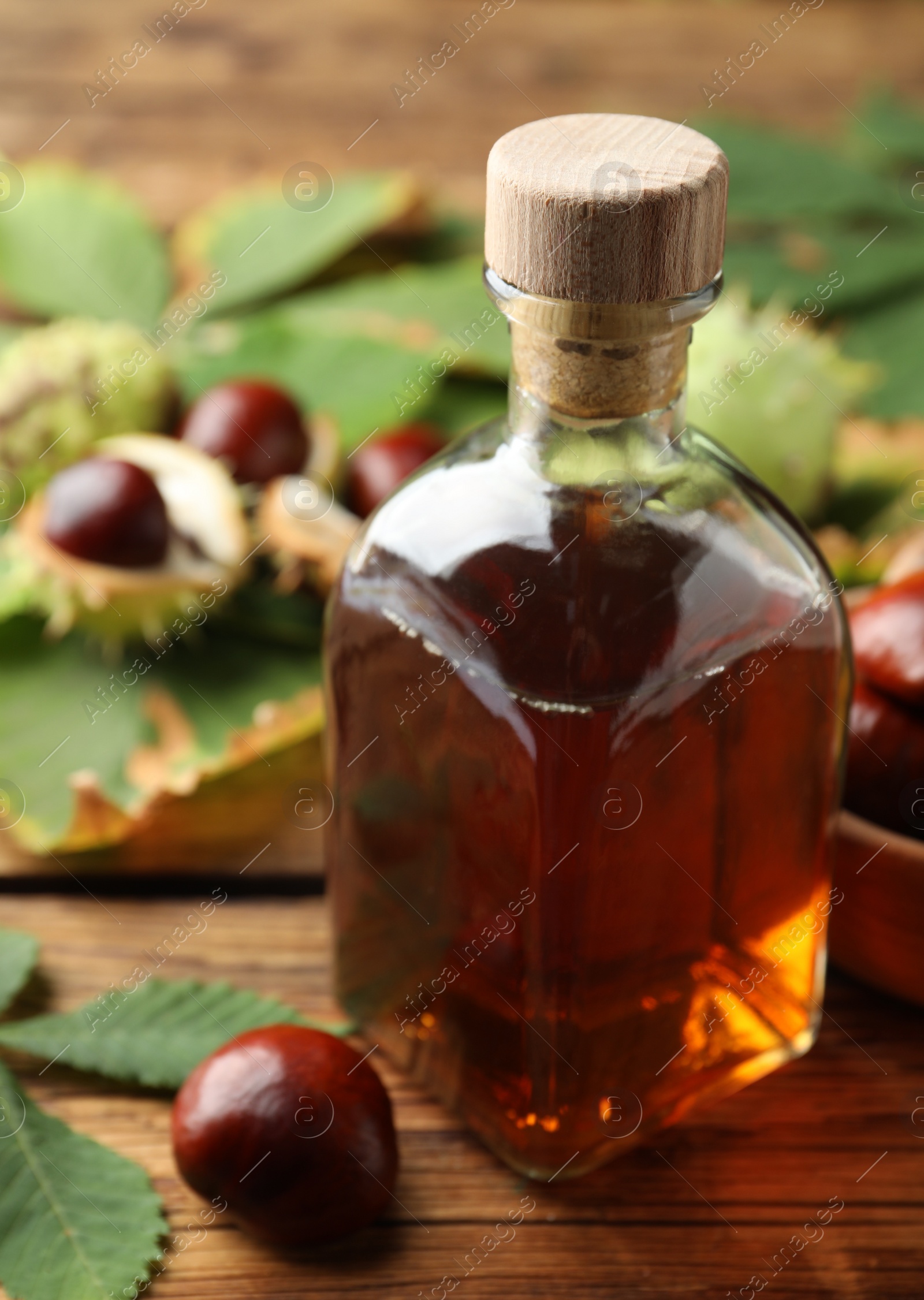 Photo of Chestnuts, leaves and bottle of essential oil on wooden table