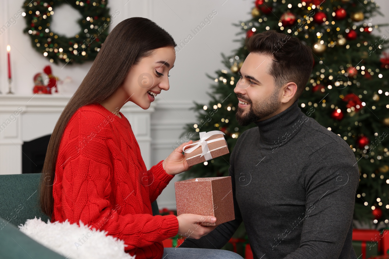Photo of Surprised young woman opening Christmas gift from her boyfriend at home