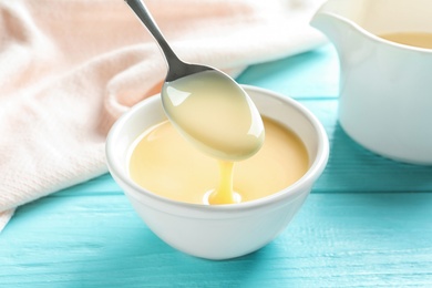 Photo of Spoon of pouring condensed milk over bowl on table. Dairy products