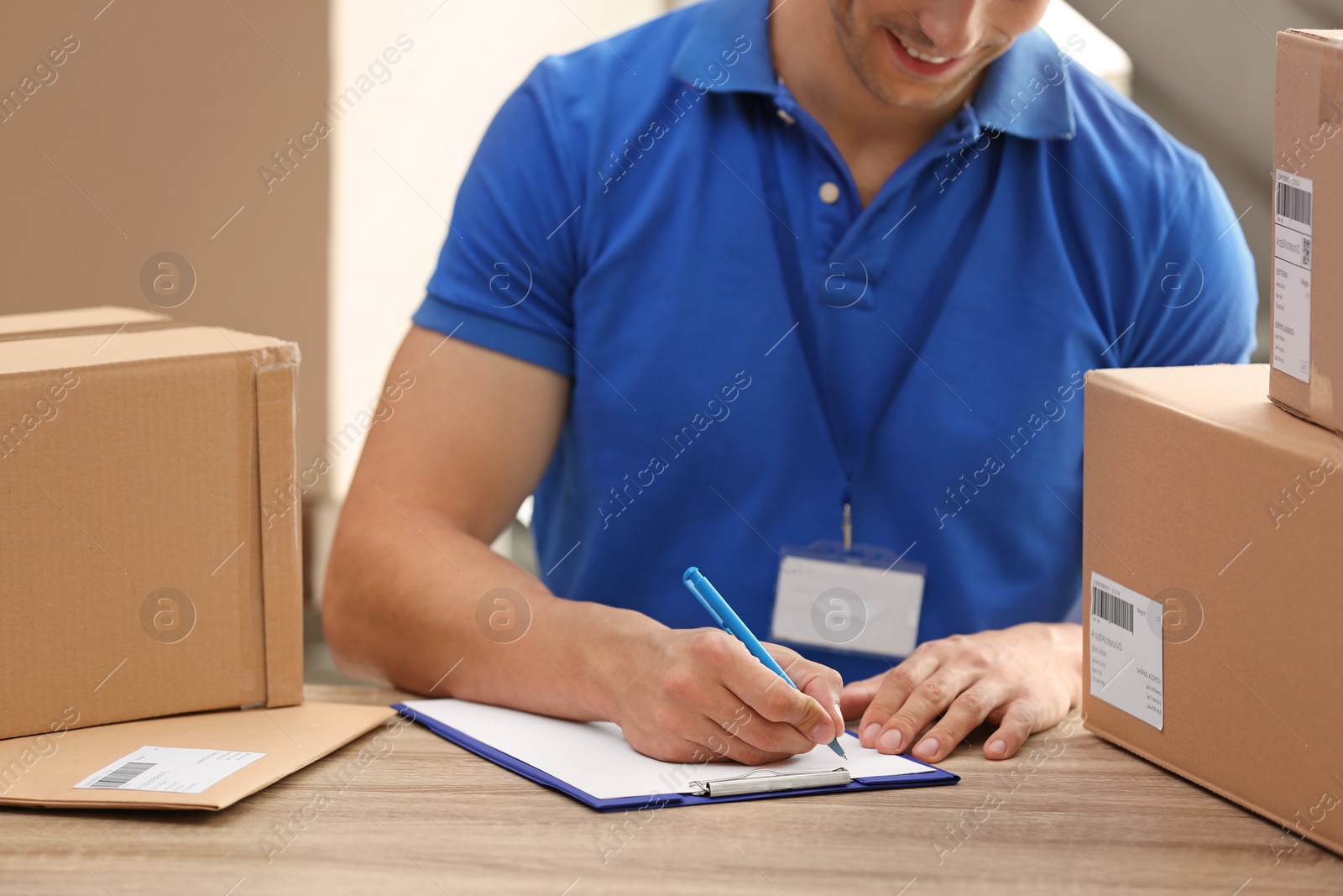 Photo of Young courier working with papers among parcels at table in delivery department