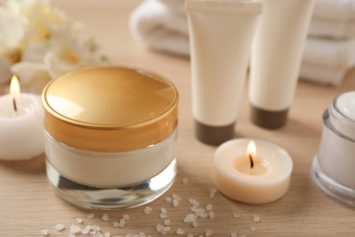 Photo of Composition with skin care products and candles on wooden table, closeup