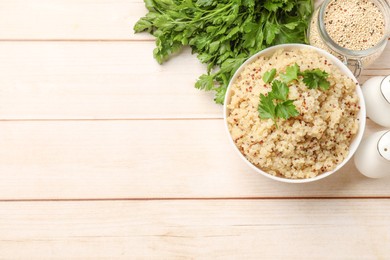 Photo of Tasty quinoa porridge with parsley in bowl and seeds on light wooden table, flat lay. Space for text