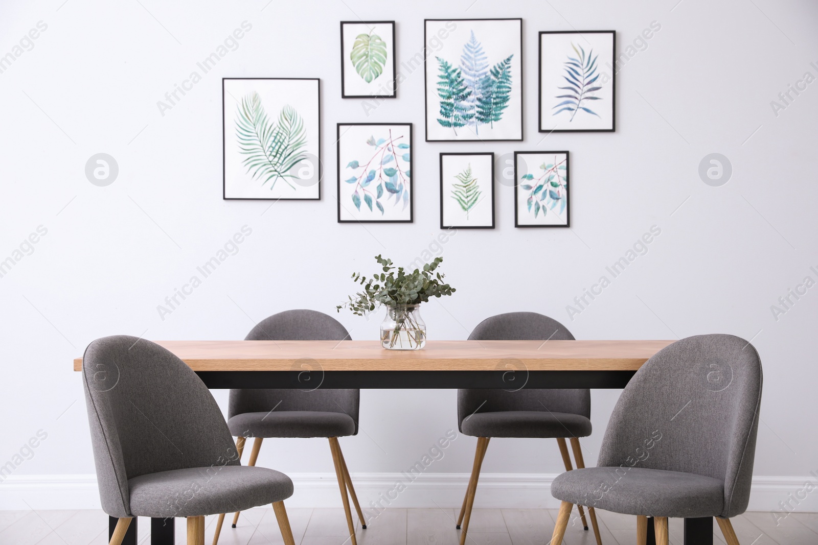 Photo of Stylish room interior with modern table, chairs and paintings of tropical leaves. Idea for design