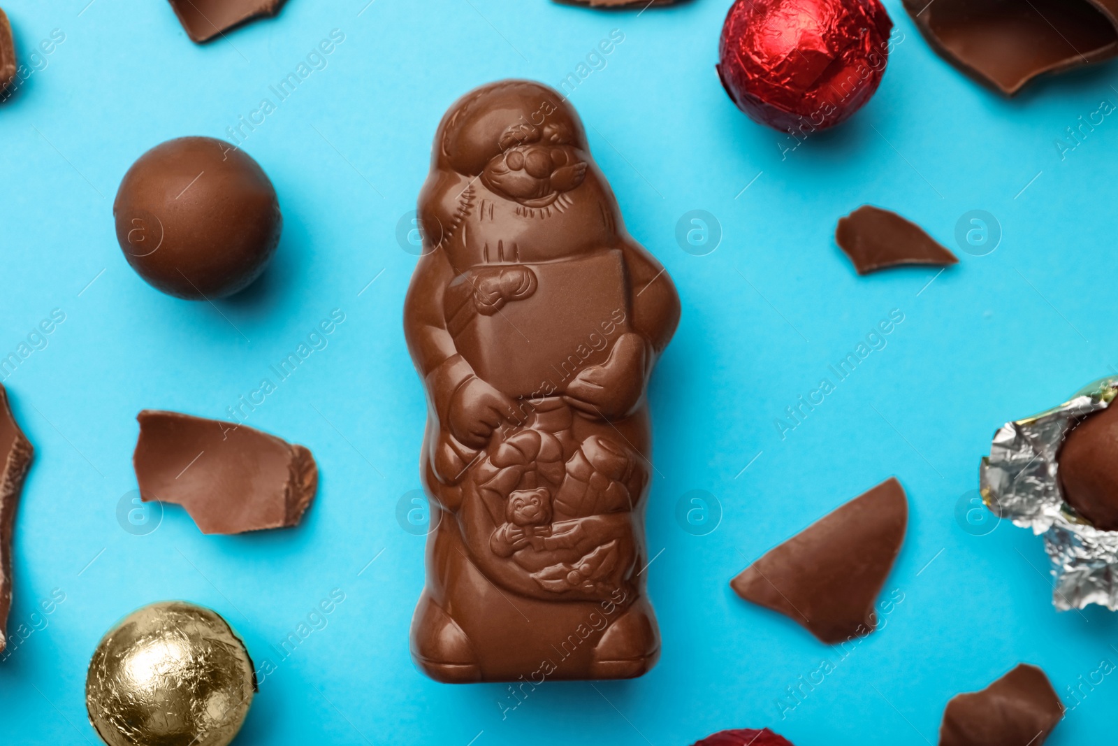 Photo of Flat lay composition with whole and broken chocolate Santa Claus candies on light blue background
