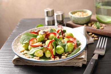 Photo of Plate of delicious salad with Brussels sprouts and roasted apples on wooden table