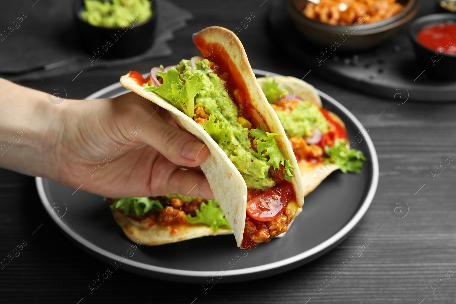 Photo of Woman holding taco with guacamole, meat and vegetables at wooden table, closeup