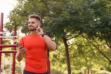Photo of Young man with wireless headphones and mobile device listening to music on sports ground. Space for text