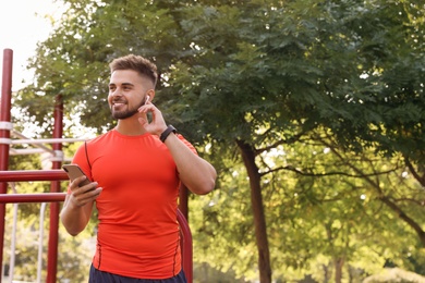 Young man with wireless headphones and mobile device listening to music on sports ground. Space for text