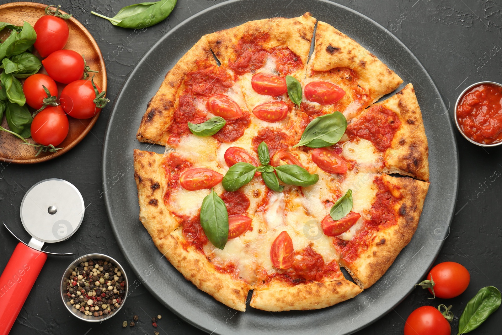 Photo of Delicious Margherita pizza, ingredients and cutter on black table, top view