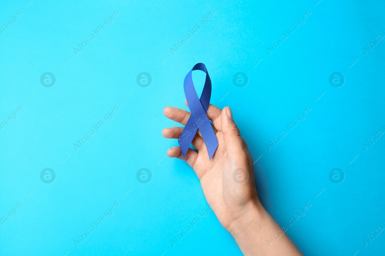 Photo of Woman holding blue awareness ribbon on color background, top view. Symbol of social and medical issues