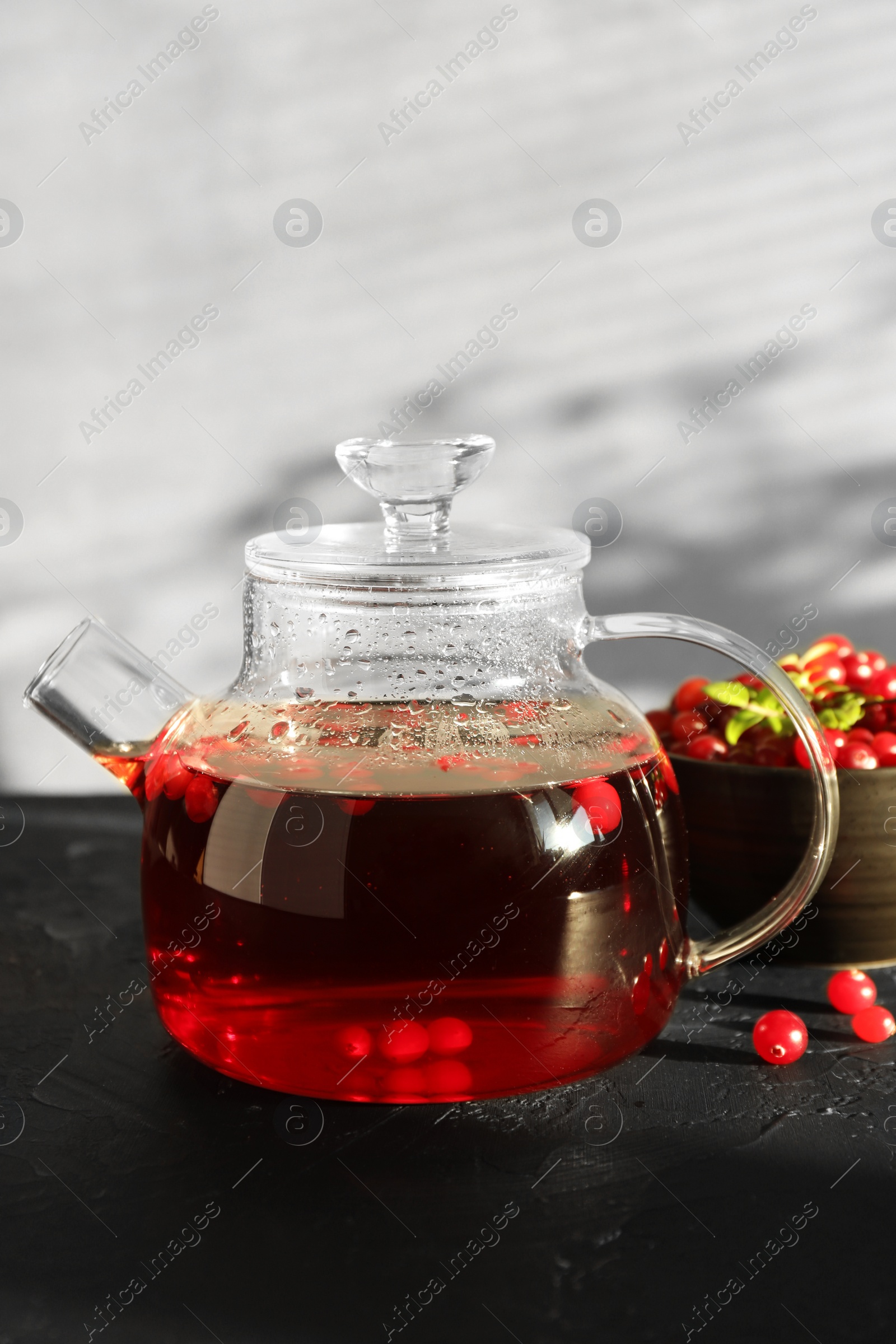 Photo of Tasty hot cranberry tea in teapot and fresh berries on black textured table