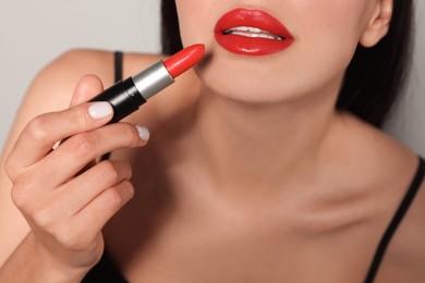 Photo of Young woman with beautiful makeup holding red lipstick on light gray background, closeup