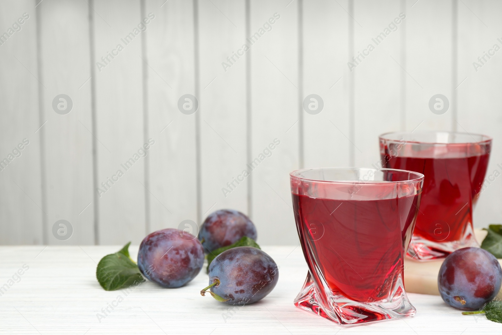 Photo of Delicious plum liquor and ripe fruits on table against white background, space for text. Homemade strong alcoholic beverage
