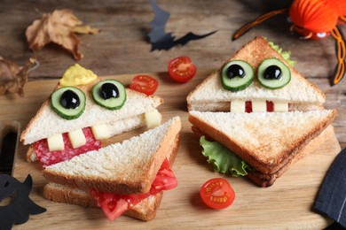 Photo of Cute monster sandwiches served on wooden board, closeup. Halloween party food