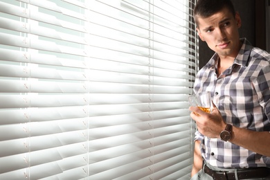 Photo of Young man with glass of whiskey near window indoors. Space for text