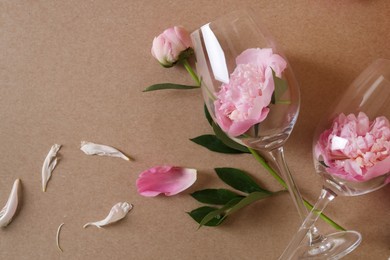 Wineglasses and beautiful pink peonies on brown background, flat lay