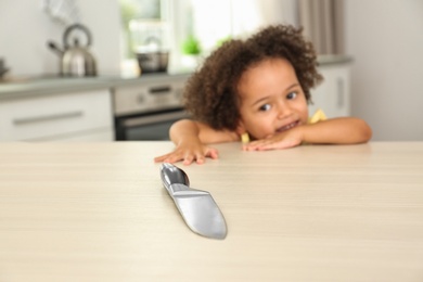 Image of Dangers in kitchen. African American girl reaching after knife at table
