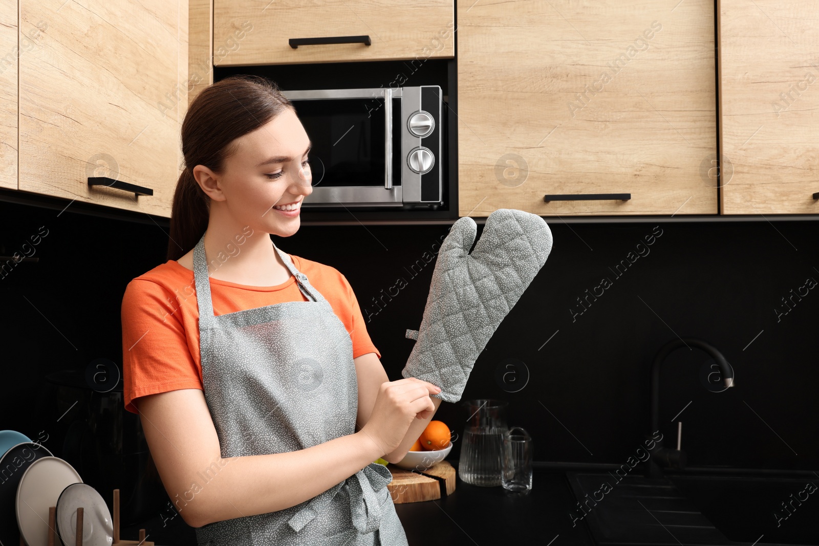 Photo of Beautiful young woman in clean apron and oven glove at kitchen