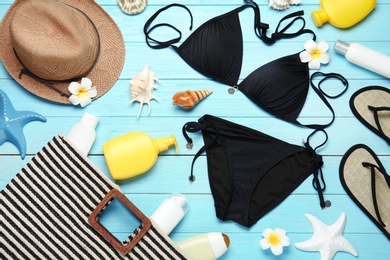 Flat lay composition with black swimsuit and beach accessories on blue wooden background