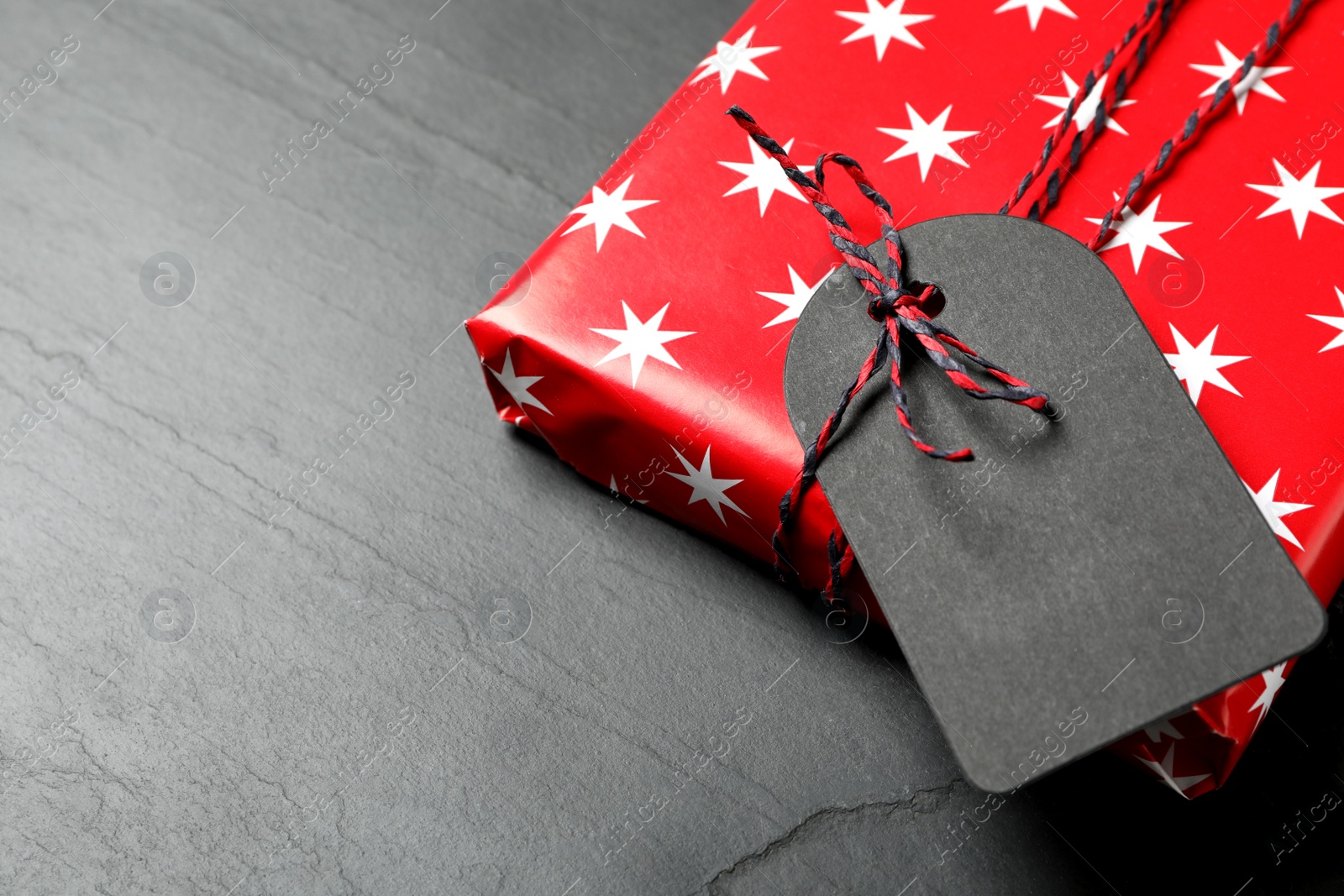 Photo of Wrapped present with blank tag on black background, closeup. Space for text