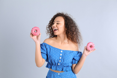 Beautiful African-American woman with donuts on light grey background