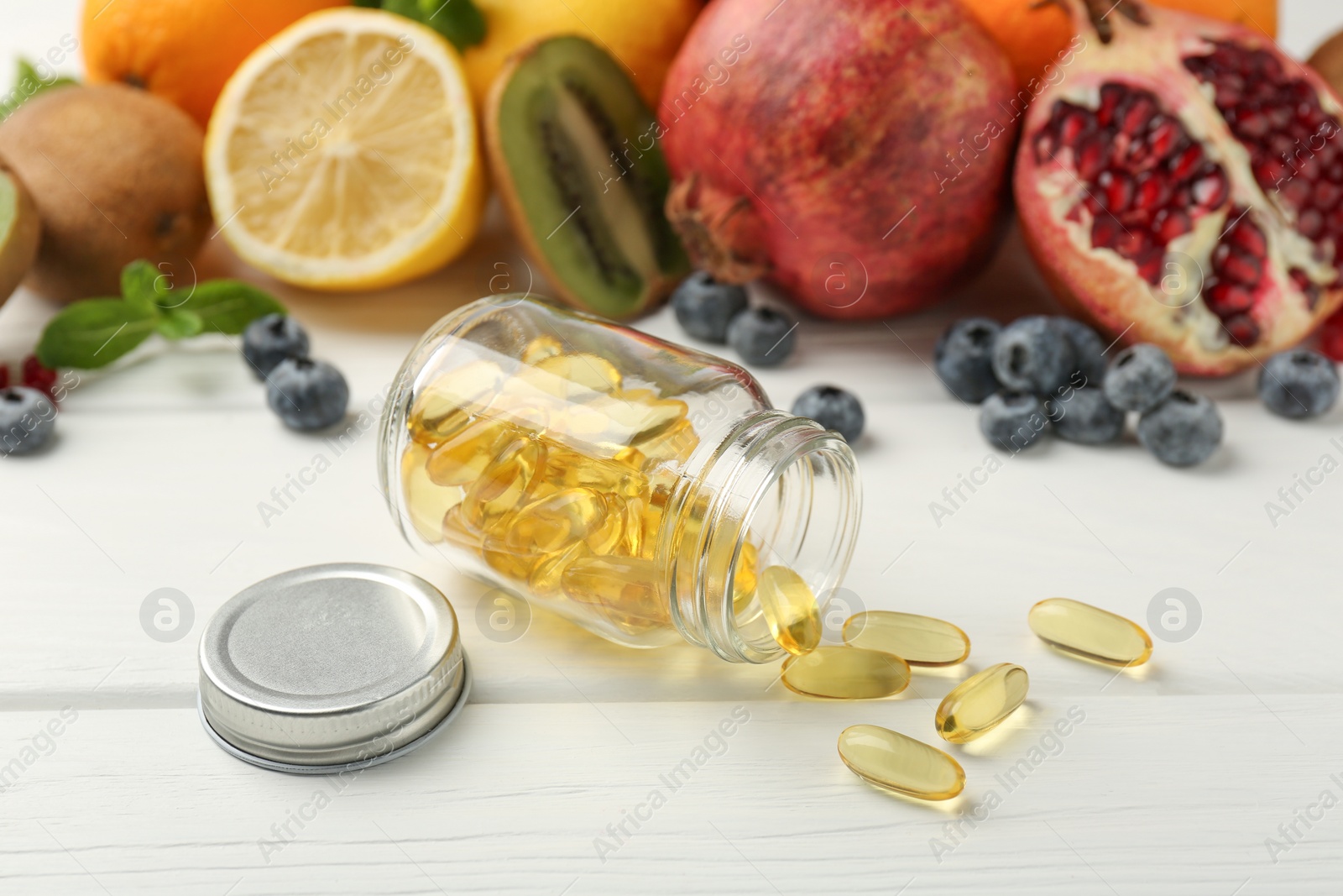 Photo of Vitamin pills, bottle and fresh fruits on white wooden table