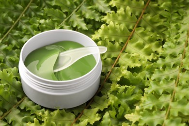Photo of Jar of under eye patches with spoon on green fern leaves, space for text. Cosmetic product