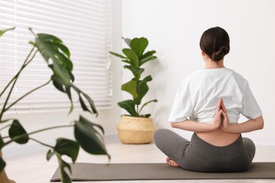 Photo of Girl practicing vajrasana with namaste behind back on mat in yoga studio