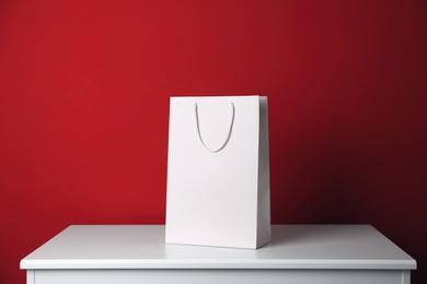 Photo of Paper shopping bag on white table against red background