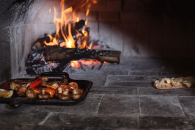 Grill pan with food and calzone near burning firewood inside of oven