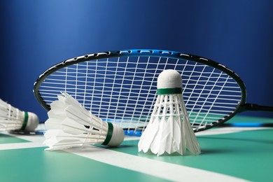 Feather badminton shuttlecocks and racket on green table against blue background, closeup