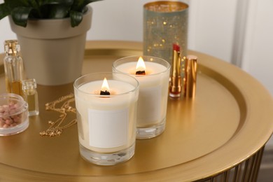 Burning soy candles, cosmetics and stylish accessories on table indoors