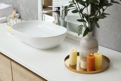 Beautiful plant in vase and burning candles near vessel sink and mirror on bathroom vanity