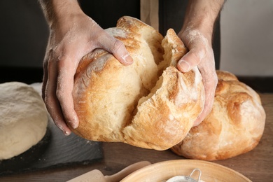 Photo of Male baker holding loaf of bread over table, closeup