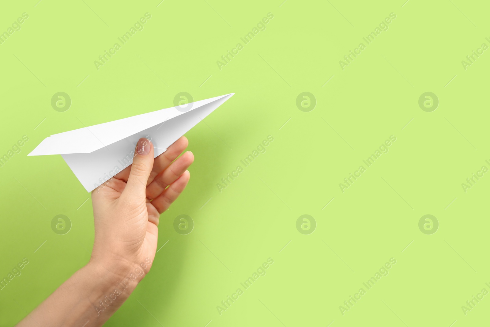 Photo of Woman holding paper plane on green background, closeup. Space for text