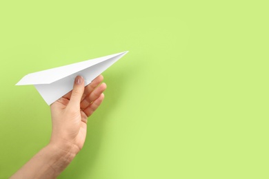 Woman holding paper plane on green background, closeup. Space for text