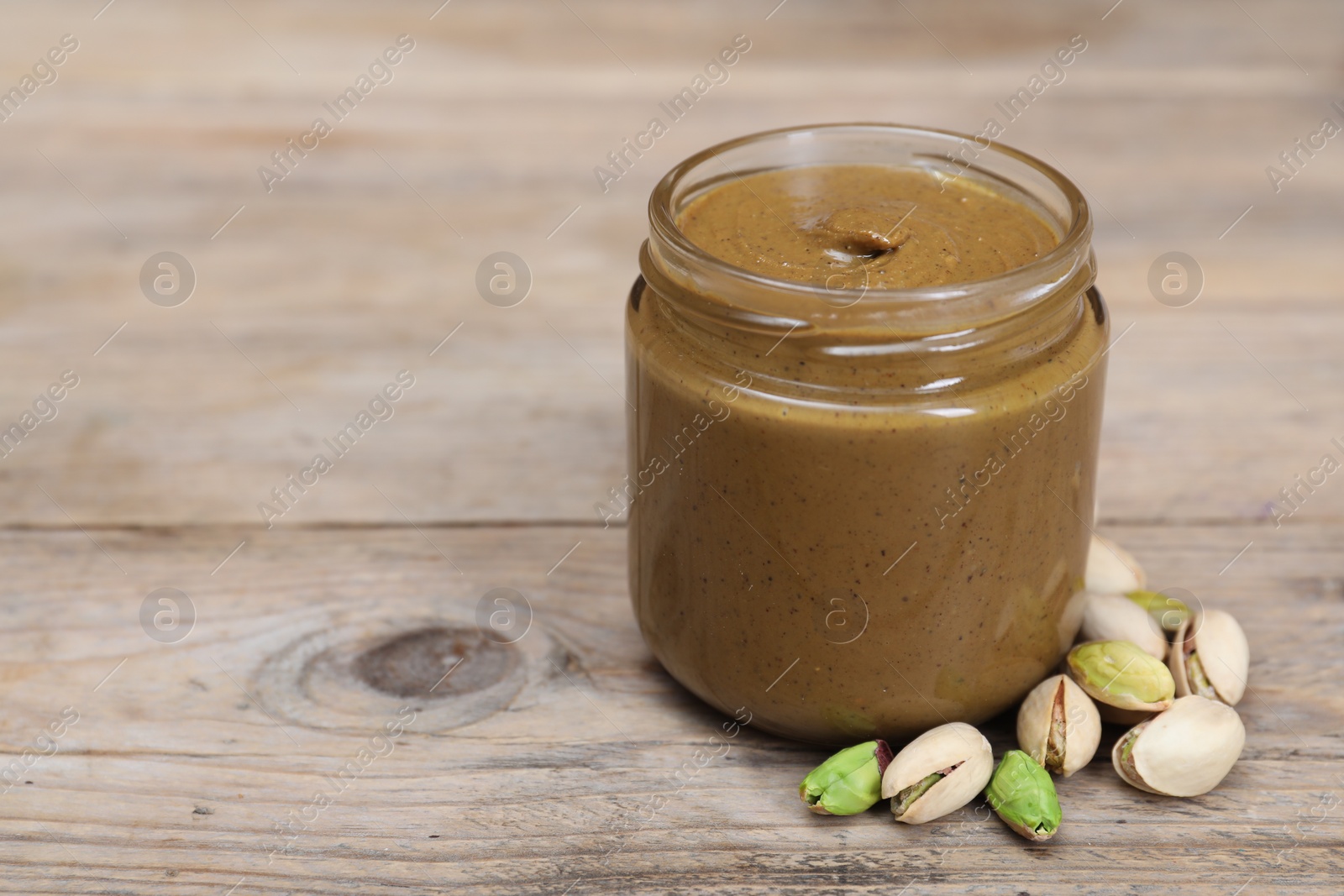 Photo of Tasty nut paste in jar and pistachios on wooden table, closeup. Space for text