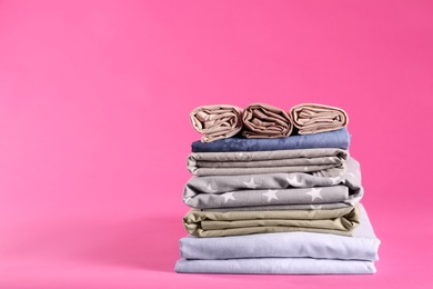 Stack of clean bed sheets on pink background. Space for text