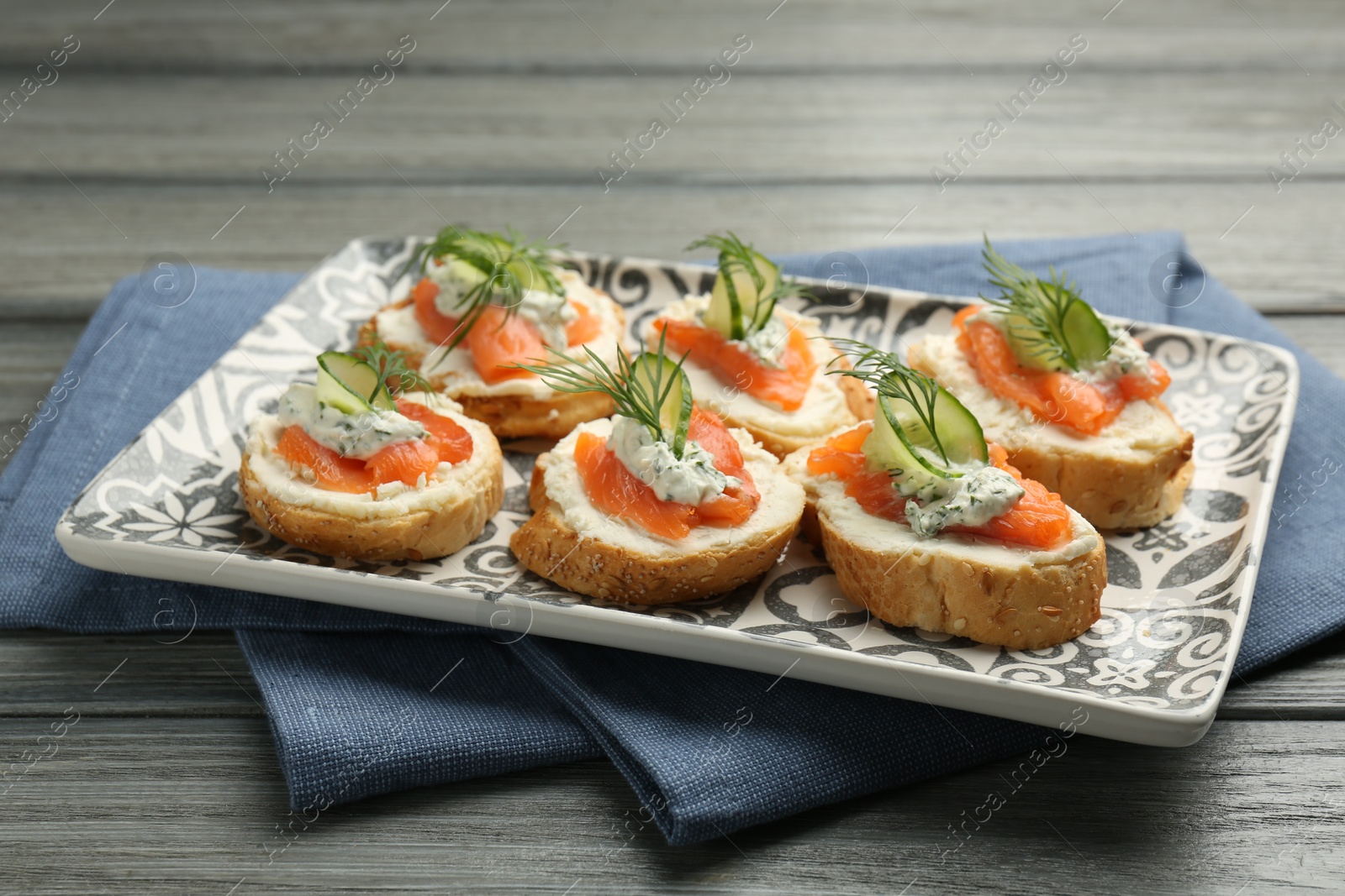 Photo of Tasty canapes with salmon, cucumber, cream cheese and dill on wooden table