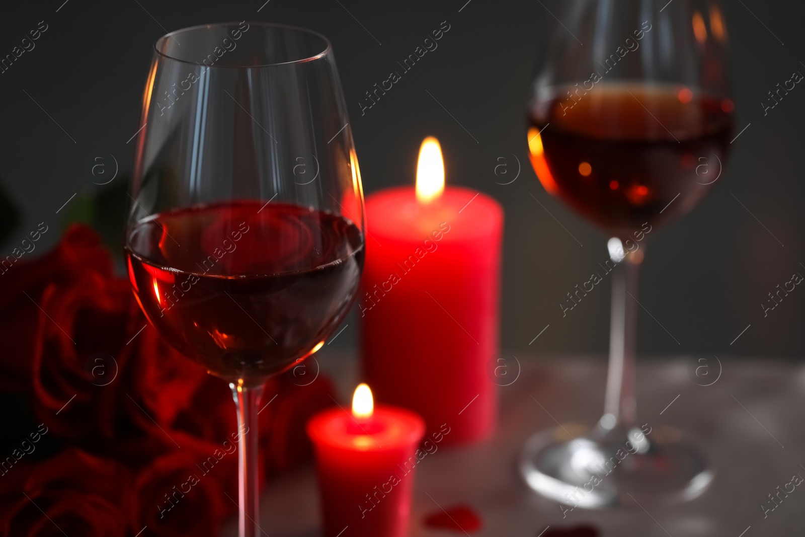 Photo of Romantic table setting with glasses of red wine, burning candles and rose flowers against blurred background