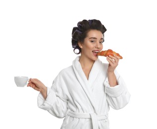 Photo of Young woman in bathrobe with hair curlers having breakfast on white background