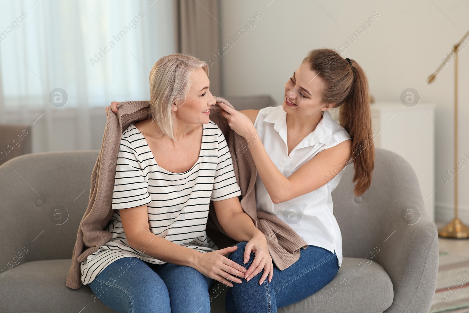 Photo of Young woman covering her mother with warm cardigan at home. Family help